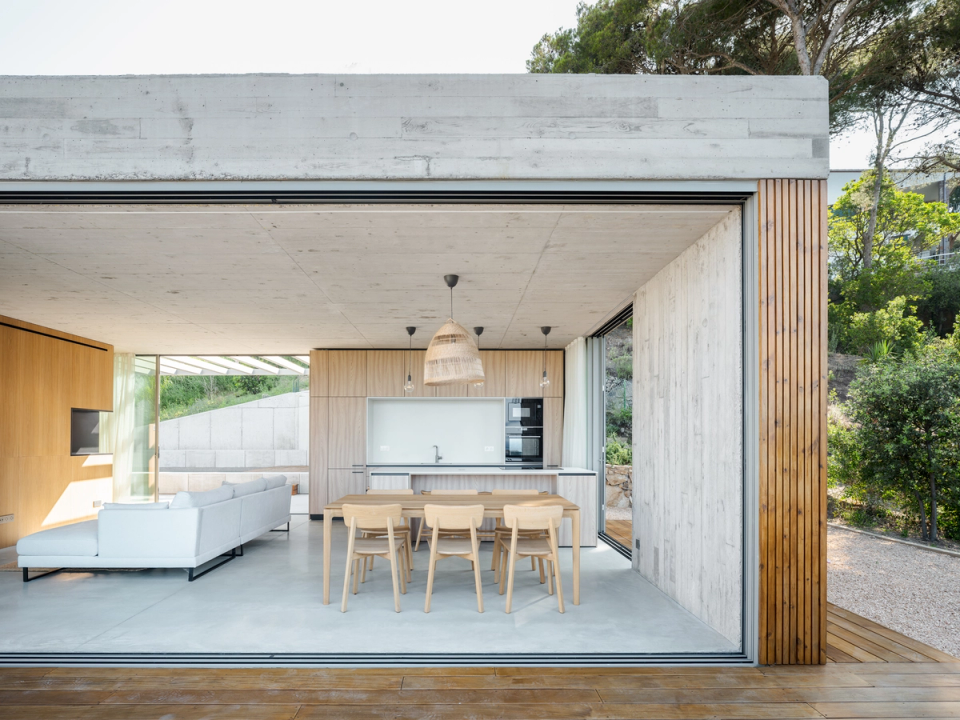 This single-family home in Begur embraces serene and functional architecture, with outdoor spaces conceived as a natural extension of the interior. The combination of exposed concrete, wood cladding, and large openings creates a contemporary and elegant image, while the metal pergola and the direct relationship with the pool provide comfort, natural light, and a fully Mediterranean living experience.