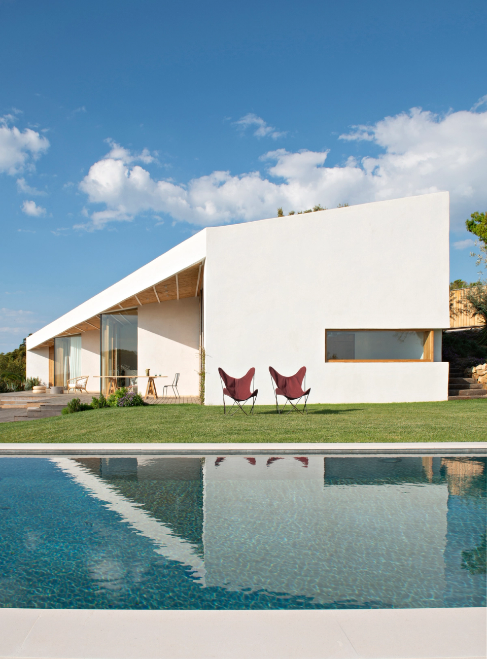 Detached house integrated into a Mediterranean natural environment, featuring minimalist architecture that dialogues with the existing vegetation and coastal landscape. White façades, vertical openings and the presence of trees provide natural shade, privacy and a harmonious connection between the home and nature.