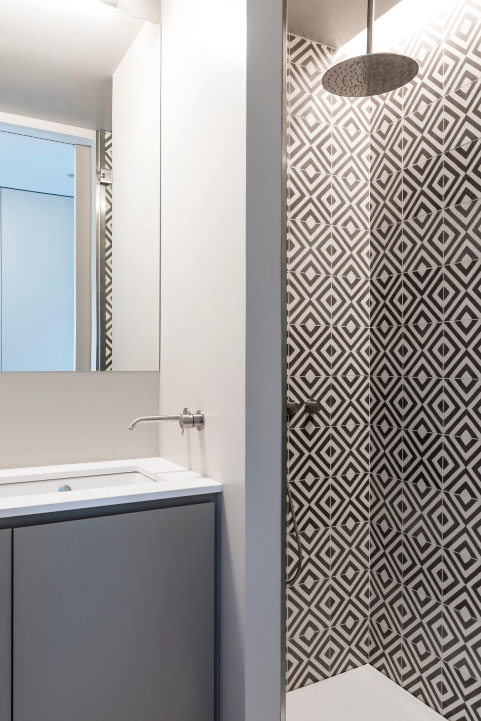 Interior renovation of a modern bathroom with open shower, black-and-white geometric tiles, and minimalist gray-toned furniture, creating an elegant, functional, and contemporary space