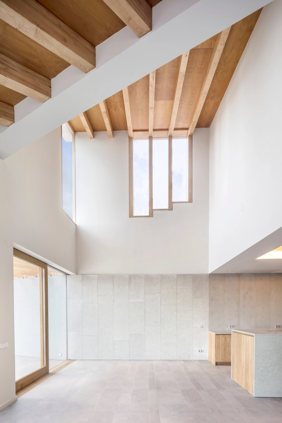 Interior of a detached single-family home with contemporary architecture based on spacious areas, double-height ceilings, and abundant natural light. Sloped ceilings with exposed wood finishes and vertical openings provide dynamism and warmth, while the combination of neutral materials and natural textures reinforces the elegance and comfort of the space.