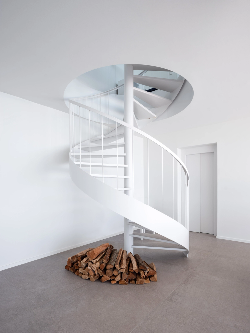 Interior of a minimalist detached single-family home where the helical staircase becomes the main feature of the space. The combination of neutral tones, natural light, and organic forms creates a sense of spaciousness and visual continuity, reinforcing an elegant and functional contemporary architecture. The use of white in the structure and surfaces enhances interior brightness and creates a serene, sophisticated, and timeless atmosphere.