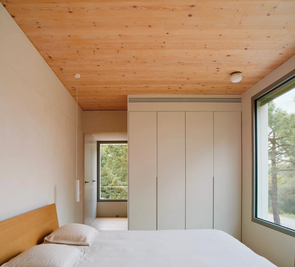 House in Girona with a bright bedroom connected to the rest of the home through interior and exterior circulation spaces. This house in Girona combines natural wood, large windows, and functional spaces to create a warm, calm, and comfortable atmosphere