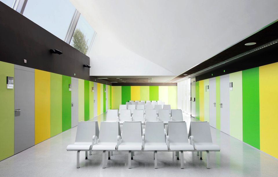 Interior of the Sant Vicenç Health Center with large glazed openings that strengthen the relationship between architecture and landscape. The presence of the existing tree becomes a central element of the space, bringing naturalness, light, and visual well-being to users, while the green tones of the interior finishes contribute to creating a calm and welcoming atmosphere.