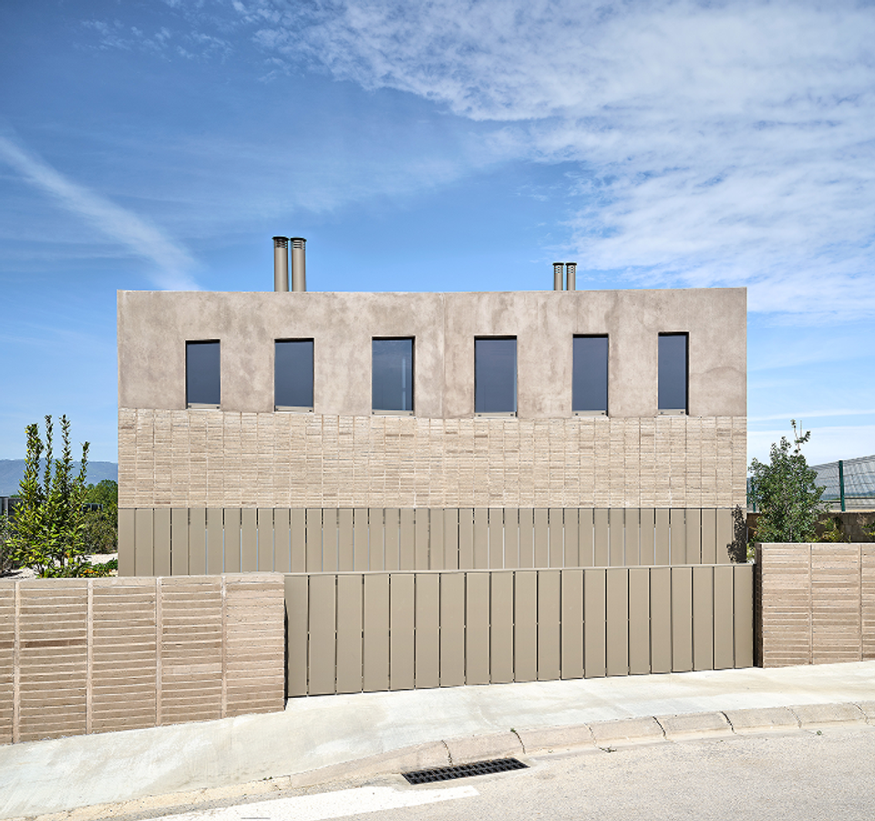 This single-family home features a contemporary façade defined by pure geometry, horizontal lines, and a balanced composition of materials and textures. The combined use of mineral cladding, light ceramics, and metallic enclosures creates an elegant and timeless architectural image, while the vertical windows add visual rhythm and encourage the entry of natural light into the interior spaces. The ensemble conveys solidity, privacy, and a clear intention of integration with the residential and landscaped surroundings.