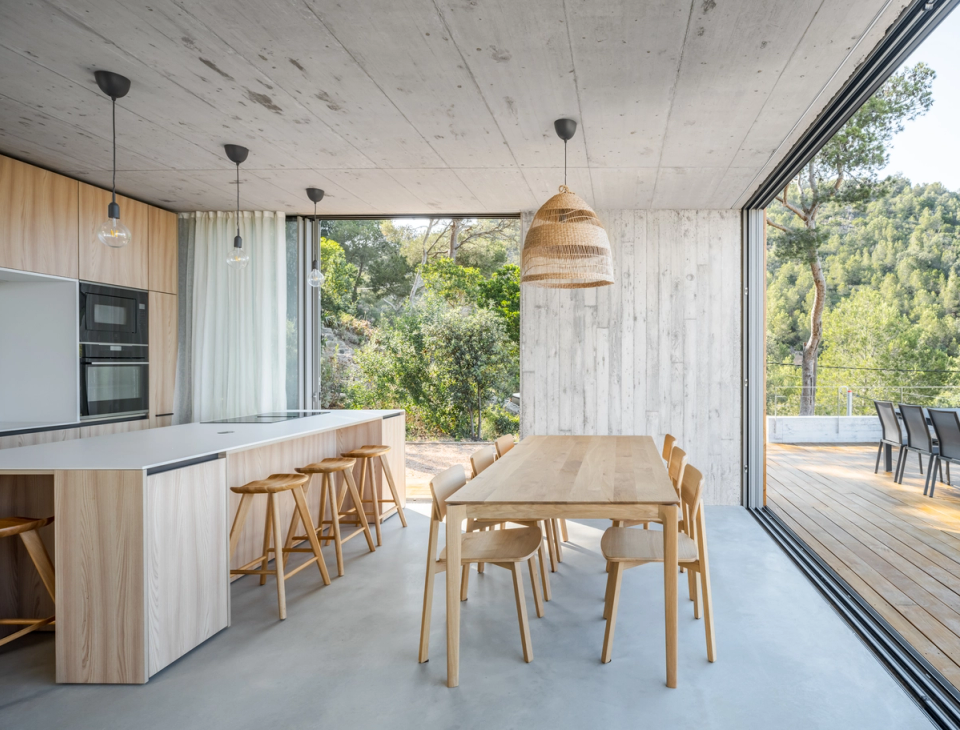 The interior space of this single-family home in Begur stands out for its spaciousness, brightness, and direct connection with the outdoors. The open kitchen, natural wood finishes, and exposed concrete create a warm and contemporary atmosphere, while the large sliding openings integrate the terrace and Mediterranean landscape into the daily living experience of the home.