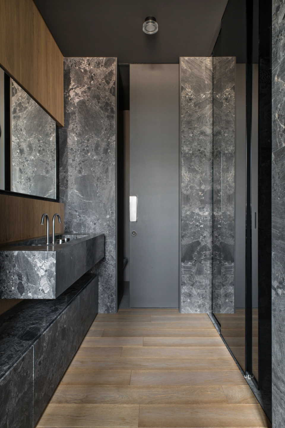 The interior renovation of this bathroom combines noble materials and contemporary finishes to create a sophisticated, elegant, and visually impactful space. The prominence of dark-toned natural stone adds texture and depth, while wooden elements and subtle lighting balance the atmosphere with a warm and refined feeling. The minimalist furniture design and clean lines enhance functionality and reinforce a modern aesthetic, transforming the bathroom into an exclusive space designed for comfort and well-being.