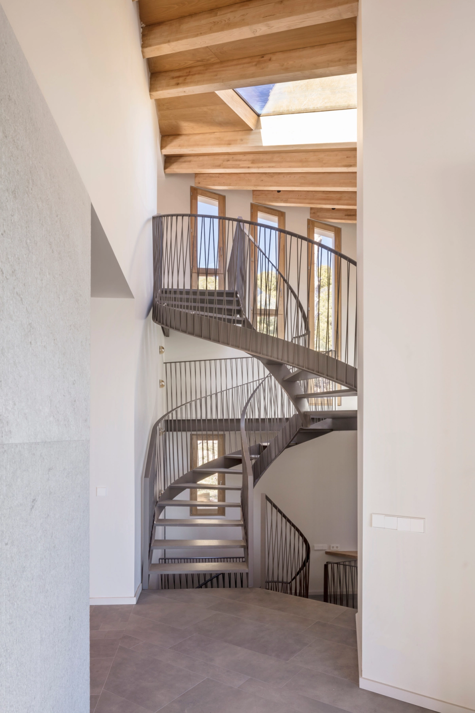 Interior of a detached single-family home with a spectacular sculptural metal staircase featuring organic lines that connects the different levels of the house, bringing dynamism, elegance, and a strong architectural identity to a spacious and bright interior.