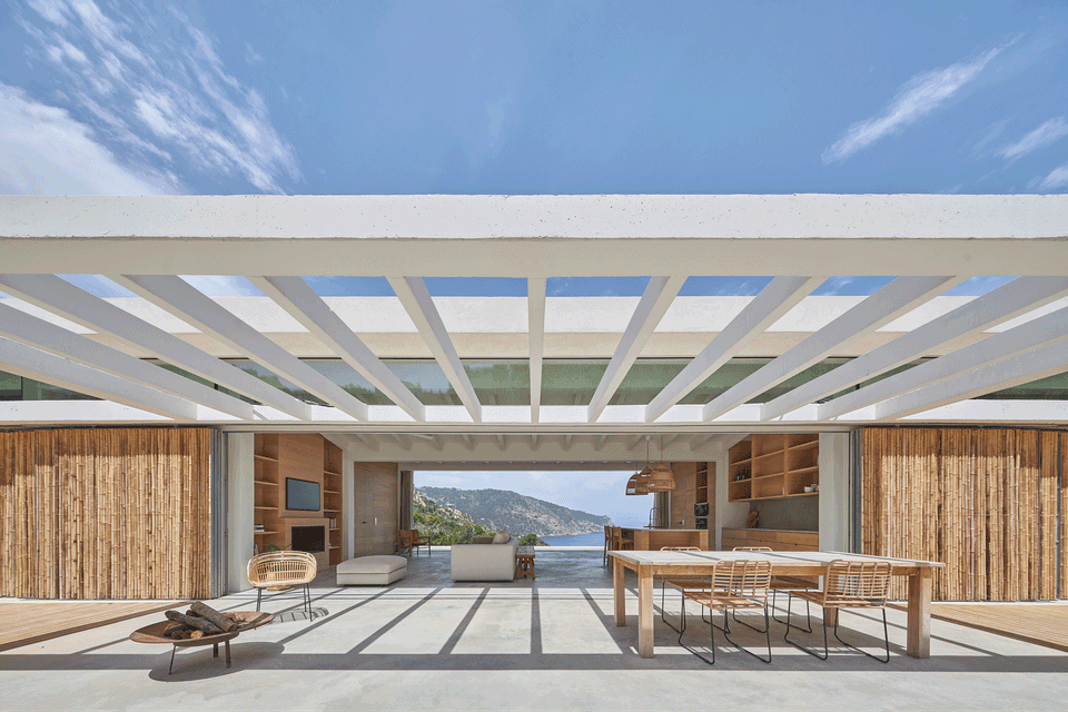 This single-family home stands out for its open and horizontal architecture, conceived to integrate naturally with the landscape and enhance sea views. The large white pergola creates a play of light and shadow that accompanies the outdoor spaces, turning the terrace into an extension of the interior area. Natural wood finishes, large sliding openings, and the direct connection between kitchen, dining room, and living area create a warm, elegant, and functional atmosphere. This single-family home embraces contemporary Mediterranean architecture, with spacious areas, noble materials, and a constant relationship between interior and exterior.