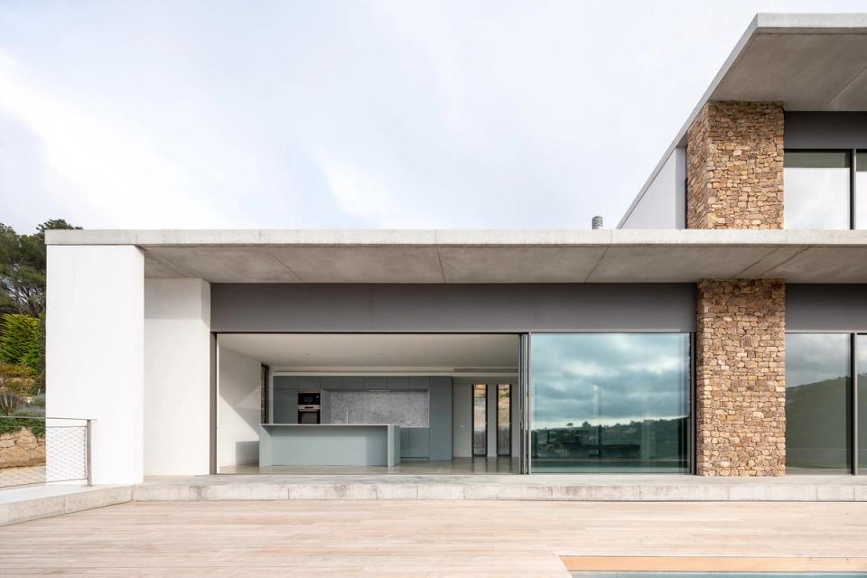 Detached single-family home with modern architecture open to the landscape. The façade combines natural stone, large windows, and clean lines to create an elegant and contemporary image. The wooden terrace and swimming pool strengthen the connection between interior spaces and the outdoor environment.