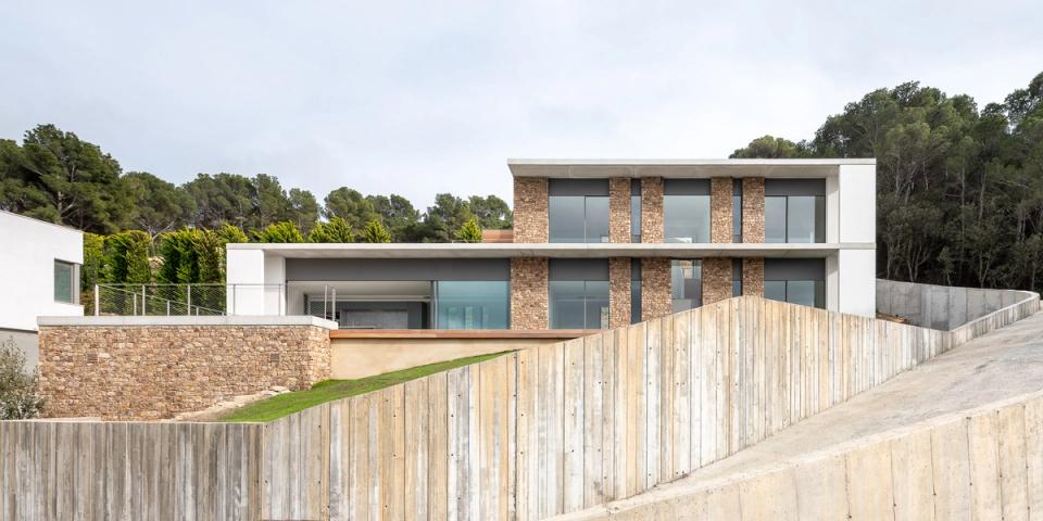 Detached single-family home elegantly integrated into the site’s topography through contemporary architecture that combines straight lines, natural materials, and balanced volumetry. The natural stone façade interacts with large windows and exposed concrete elements, creating a sober, modern image fully connected to the surrounding landscape.
