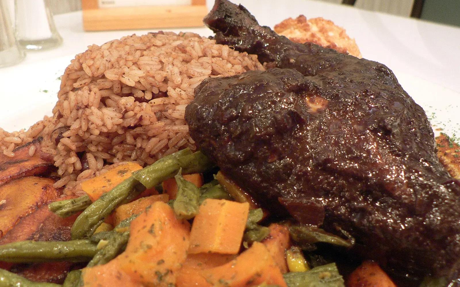 A plate of jerk chicken, rice, plantain and a biscuit