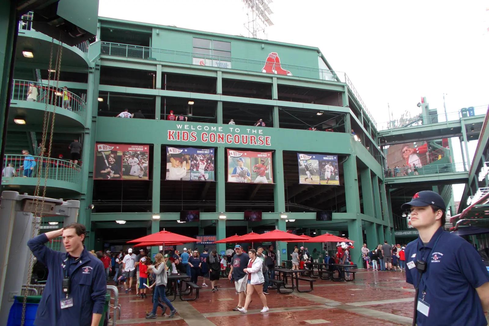 Visitors walking through the exterior concourse at Fenway Park beneath Red Sox signs