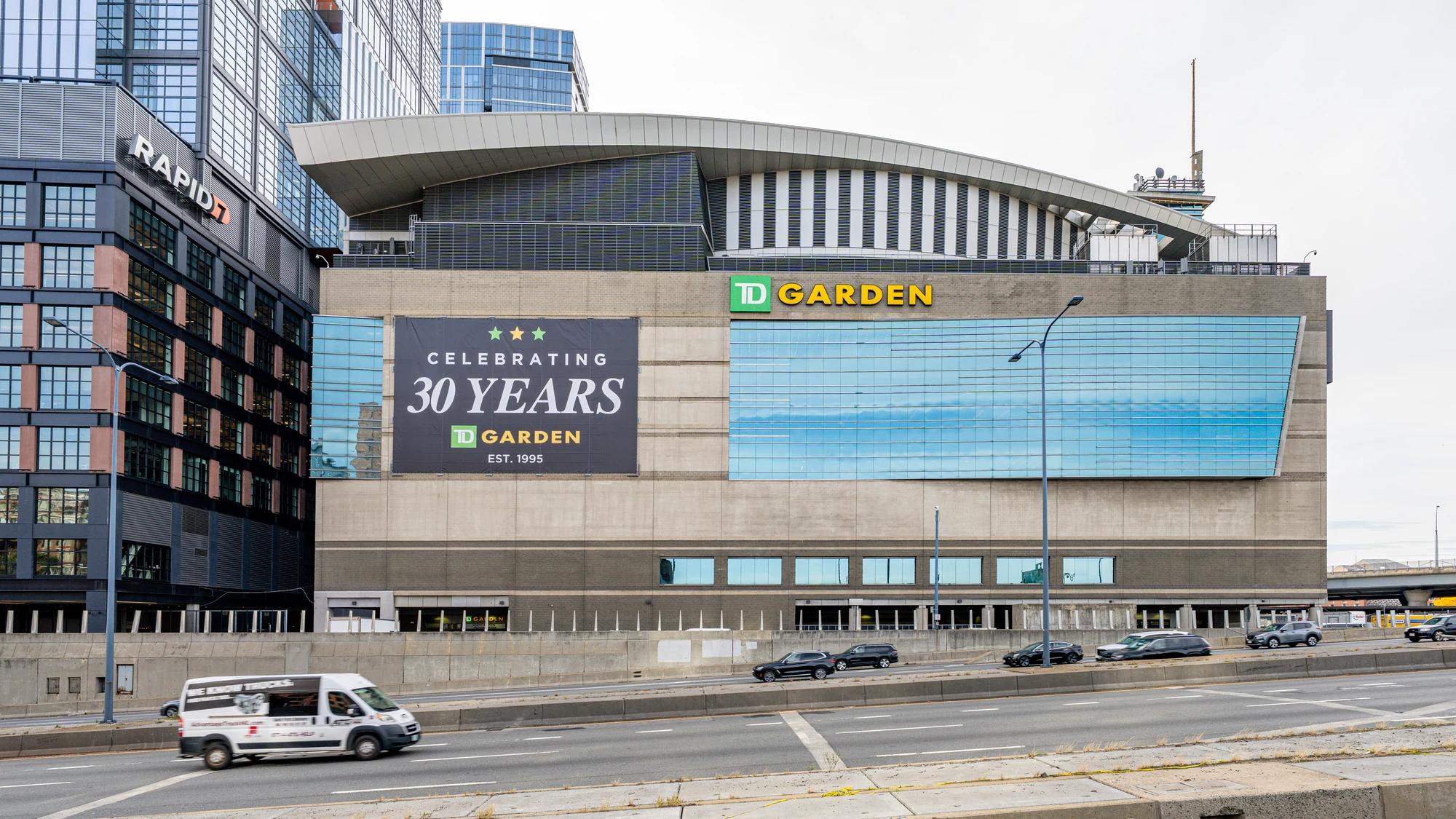 TD Garden’s exterior with its green and gold sign and a 30th-anniversary banner above Boston traffic.