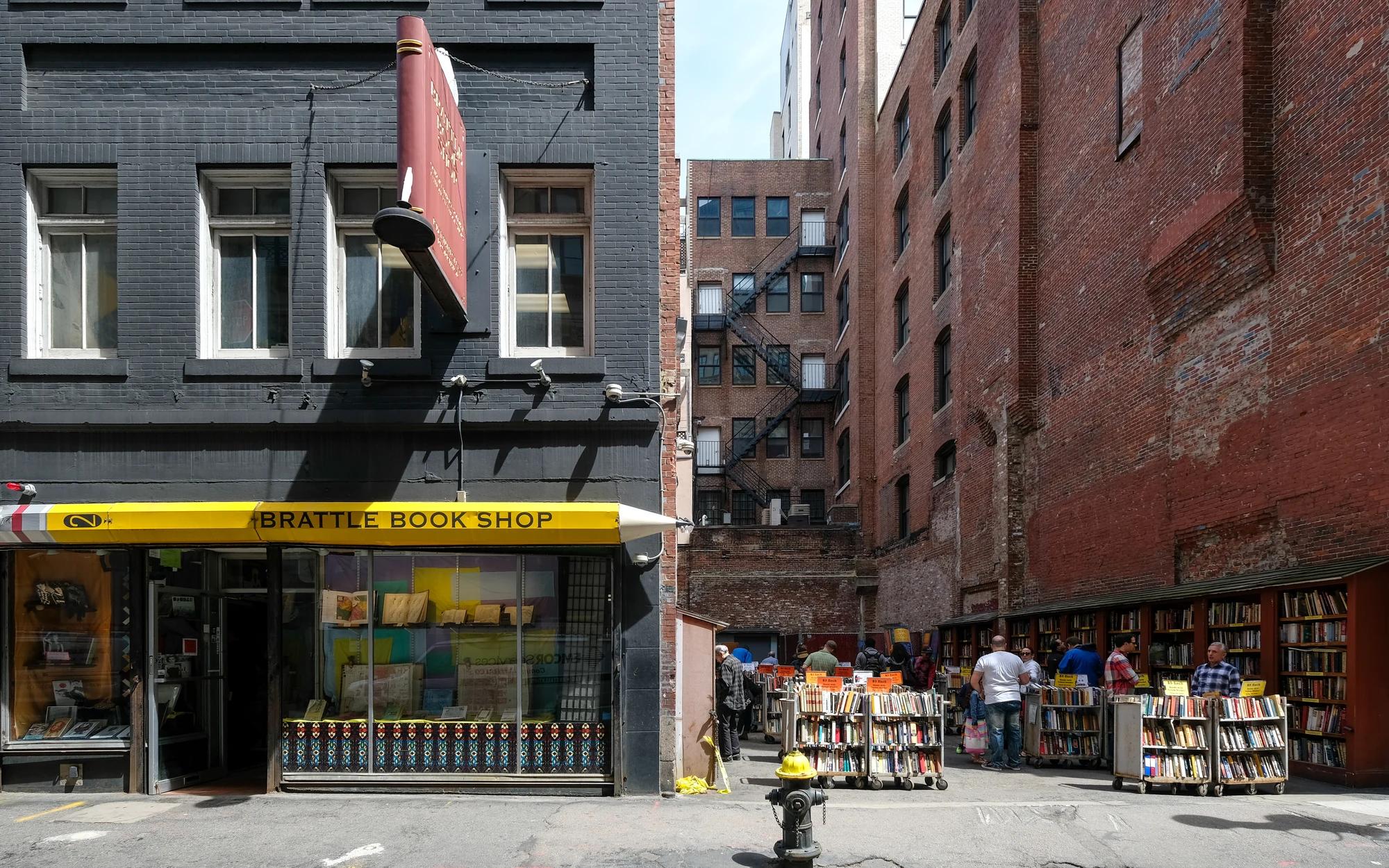 Brattle Book Shop's storefront beside outdoor shelves and carts of used books, with people browsing in the book lot