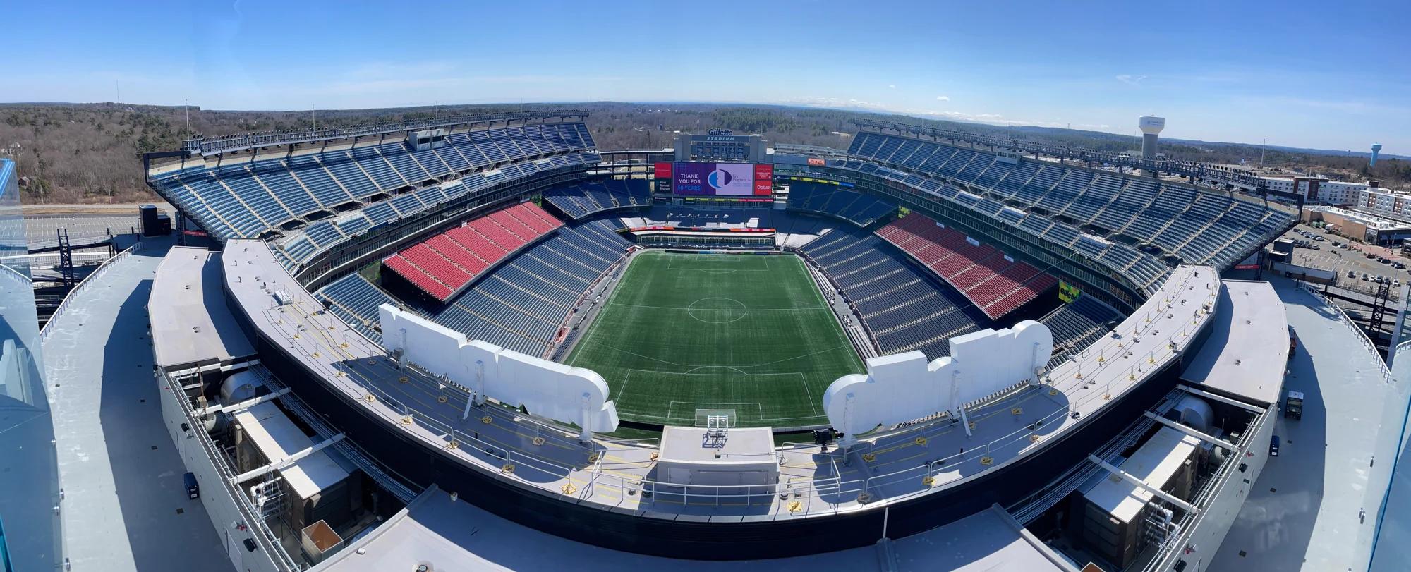 Panoramic view of Gillette Stadium with blue and red seats and a field marked for soccer.