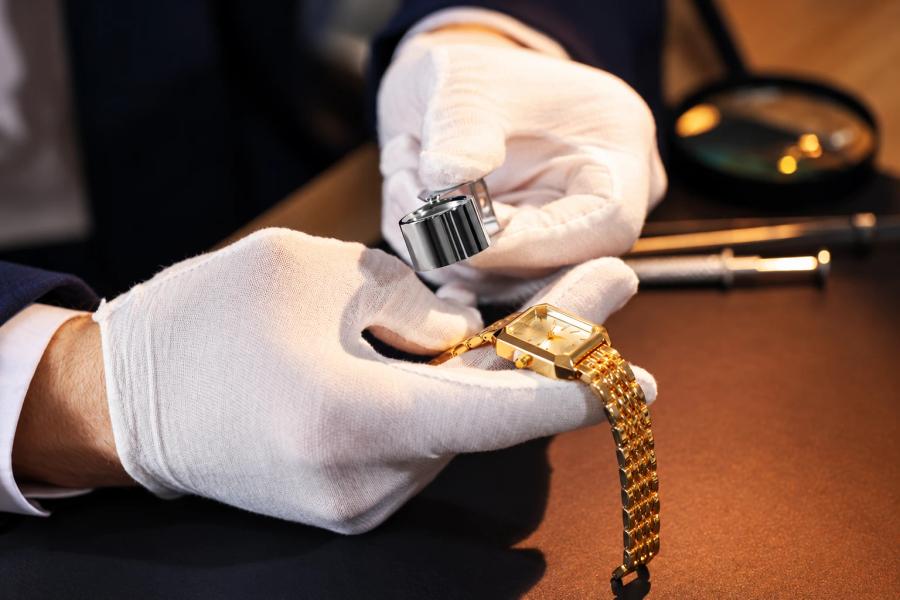 A specialist in white gloves examining a gold watch with a loupe