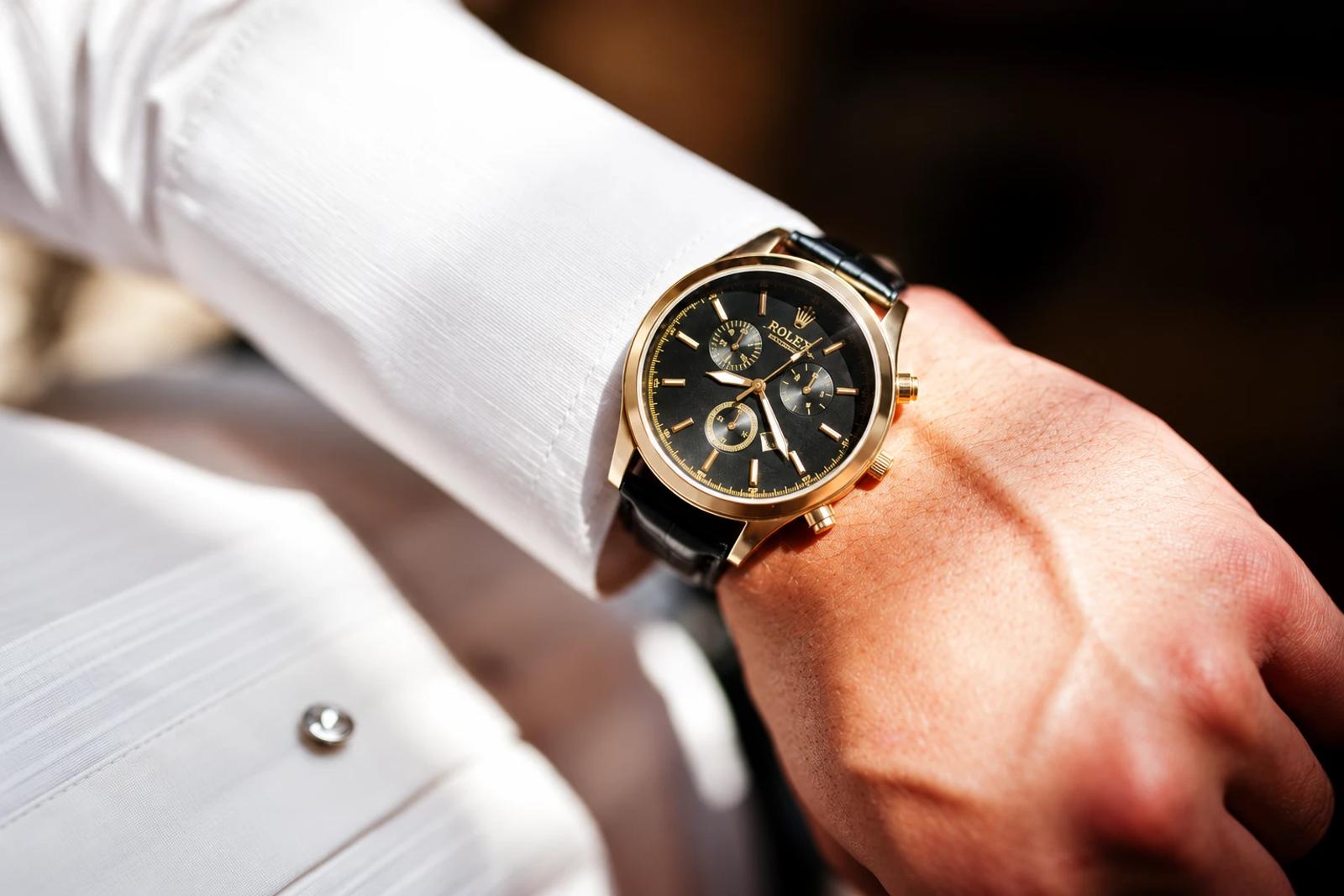 A gold Rolex chronograph on the wrist, worn with a white shirt cuff