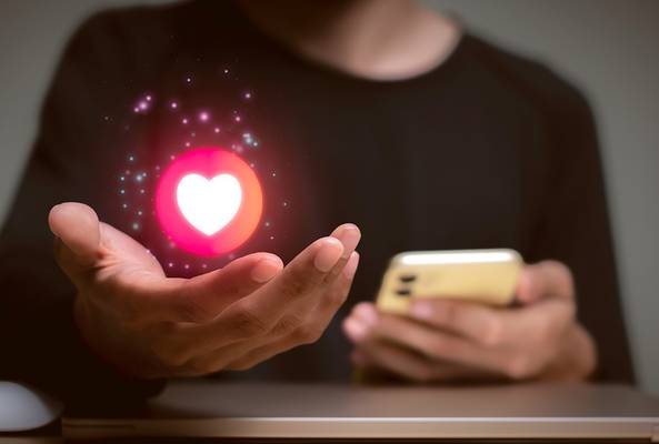 Person holding phone with glowing heart icon hovering above hand, symbolizing social media likes