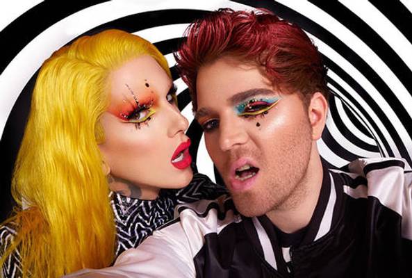 Close-up of two people with bold colorful makeup and vibrant hair against spiral background