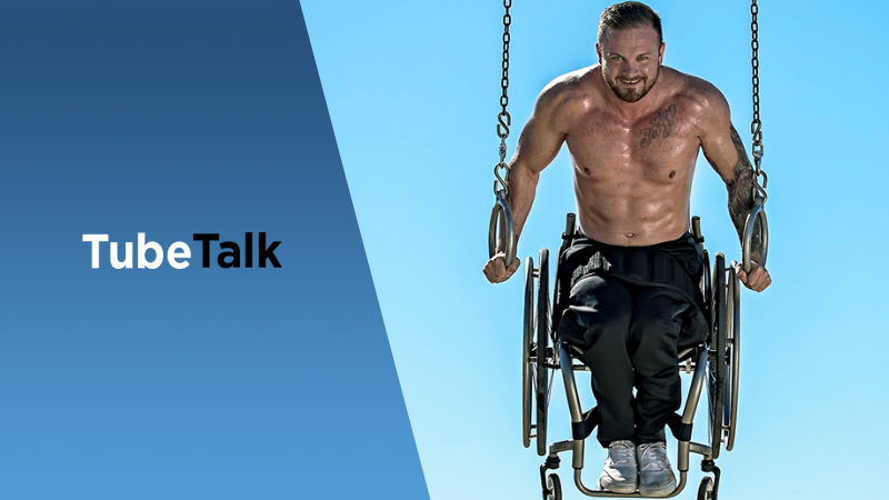 Muscular man in wheelchair using gymnastic rings outdoors with bright blue sky background.