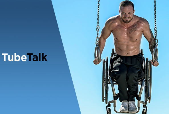 Muscular man in wheelchair using gymnastic rings outdoors with bright blue sky background.