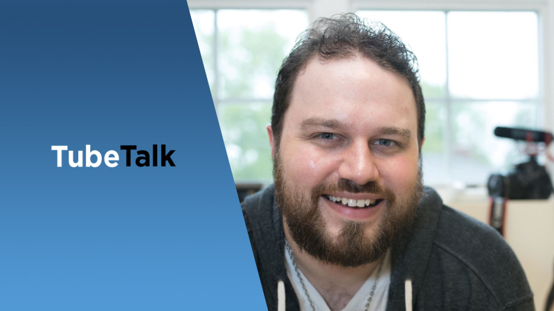 Man smiling in front of a camera with TubeTalk logo on a blue background panel