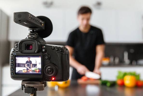 Digital camera recording a cooking video with a person chopping vegetables in kitchen