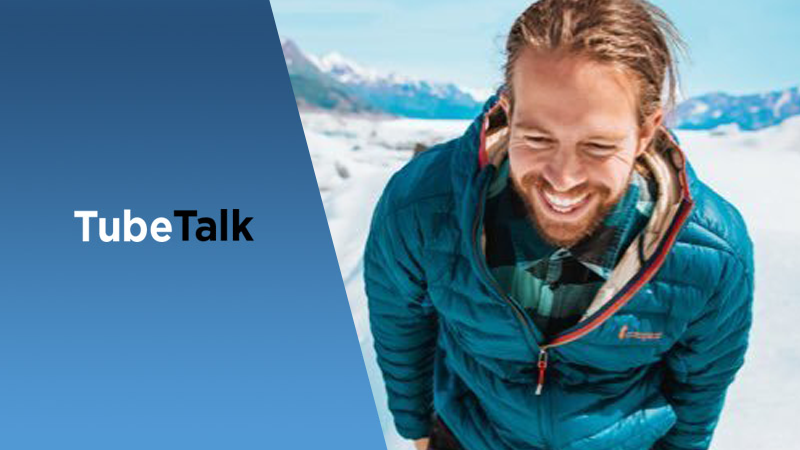 Smiling man in blue jacket outdoors on snow with TubeTalk logo on left side