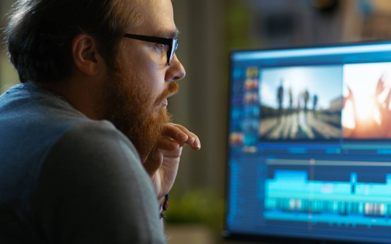 Man focused on video editing with timeline and footage on computer screen at desk
