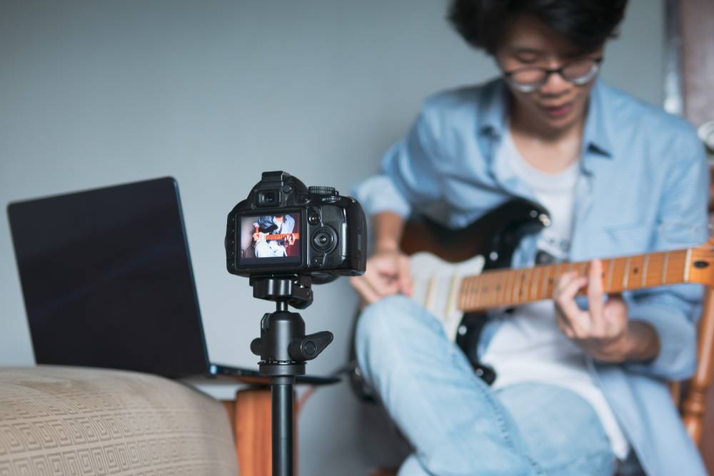 Young man recording guitar lesson with digital camera and laptop at home studio
