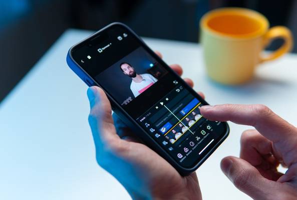 Person editing a video on a smartphone with a yellow mug in the background on table.