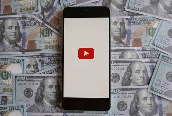 Smartphone displaying YouTube logo on screen, surrounded by US $100 bills.