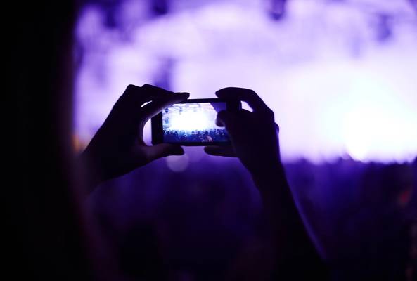 Person holding smartphone capturing a live concert with purple stage lighting effects