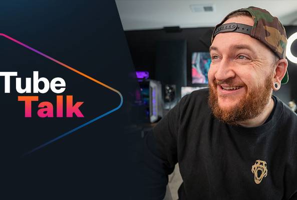 Smiling man with beard and cap in a modern studio with Tube Talk logo on screen.