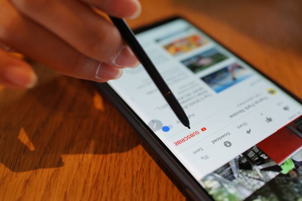 A person tapping the YouTube subscribe button on their phone