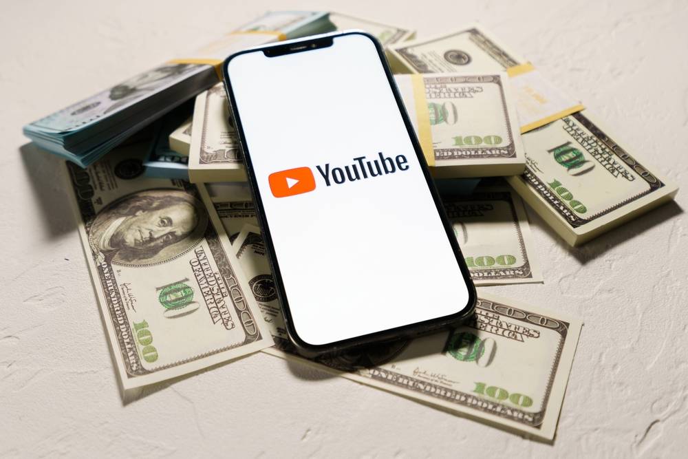 phone laying on pile of money and showing youtube logo