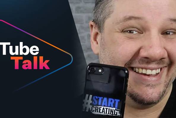 Smiling man holding phone with #StartCreating case beside Tube Talk logo on dark background
