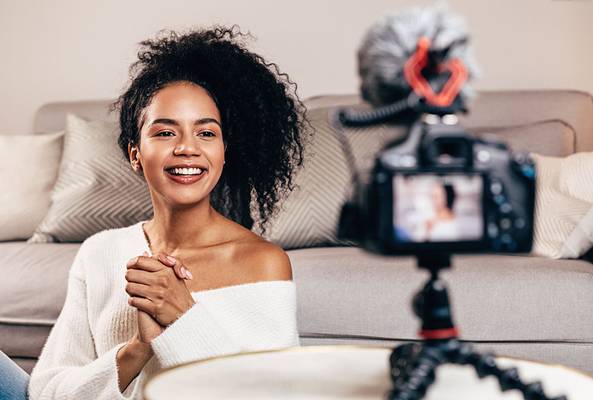 Smiling woman recording lifestyle vlog at home with camera on tripod in living room