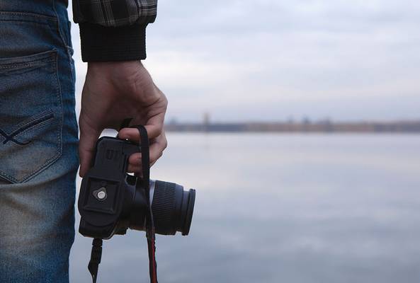 Person holding a DSLR camera by a calm lake, ready for outdoor photography session