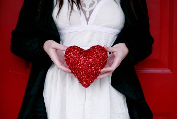 Person holding a sparkling red heart decoration against a red door background