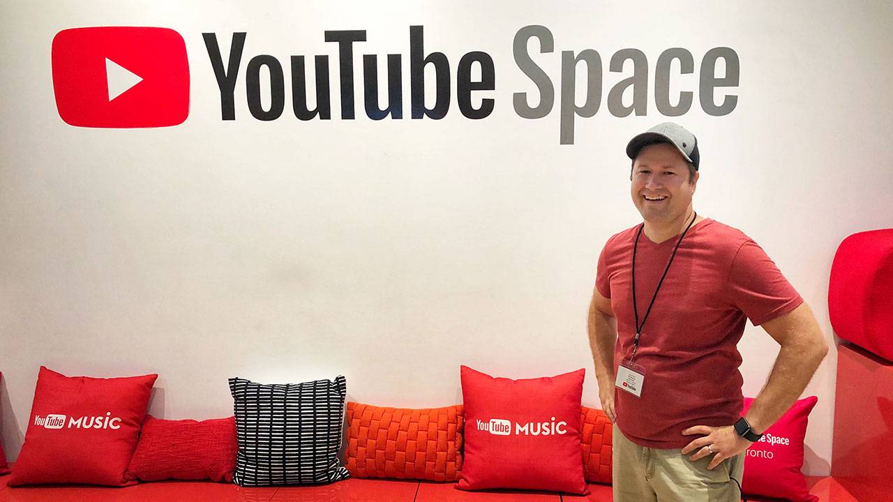 Man smiling next to YouTube Space wall and red YouTube Music pillows in studio lounge area