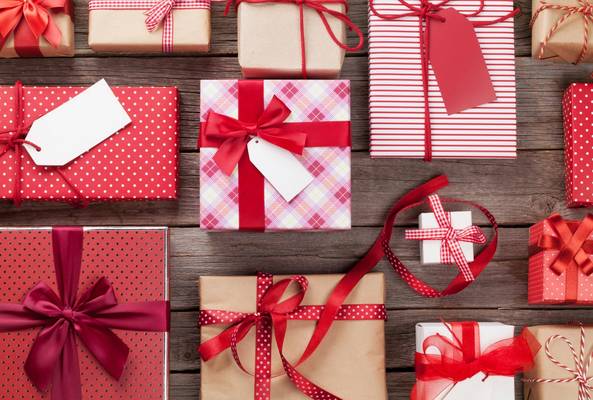 Assorted wrapped gift boxes with red ribbons and gift tags on wooden background