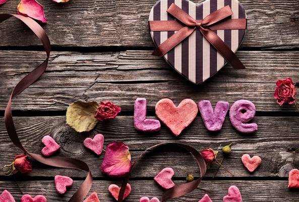 Striped heart-shaped gift box, pink heart cookies spelling love, rose petals on wood
