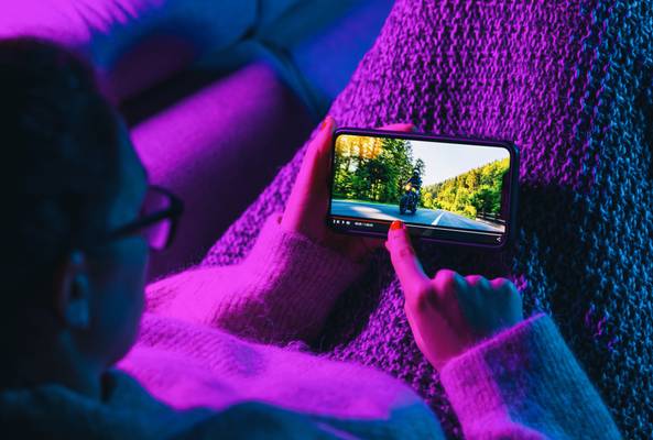 Person watching a motorcycle video on smartphone while sitting on a purple blanket indoors