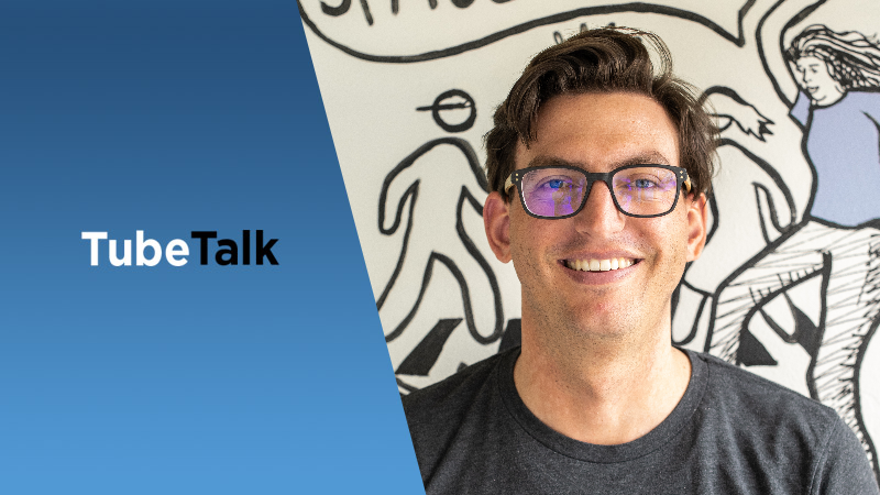 Smiling man wearing glasses with TubeTalk logo and illustrated background behind him