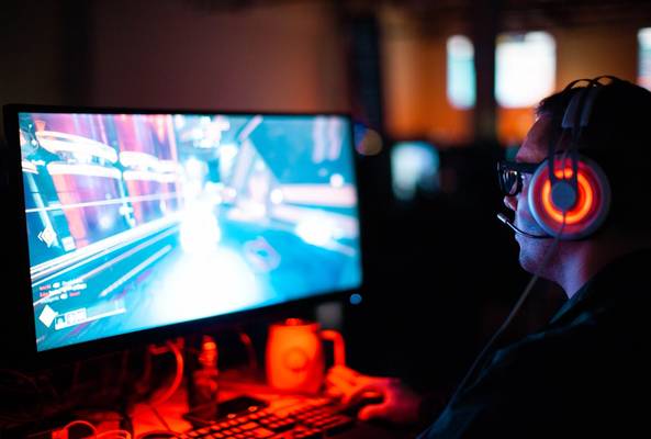 Gamer wearing headphones playing a video game on a computer in a dark room with red light