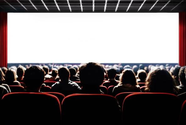 Audience watching a movie in a dark theater with red seats and a large blank screen.