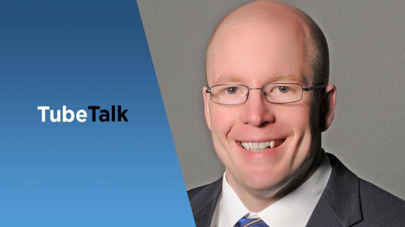 Smiling man in glasses and suit next to blue background with TubeTalk logo text.