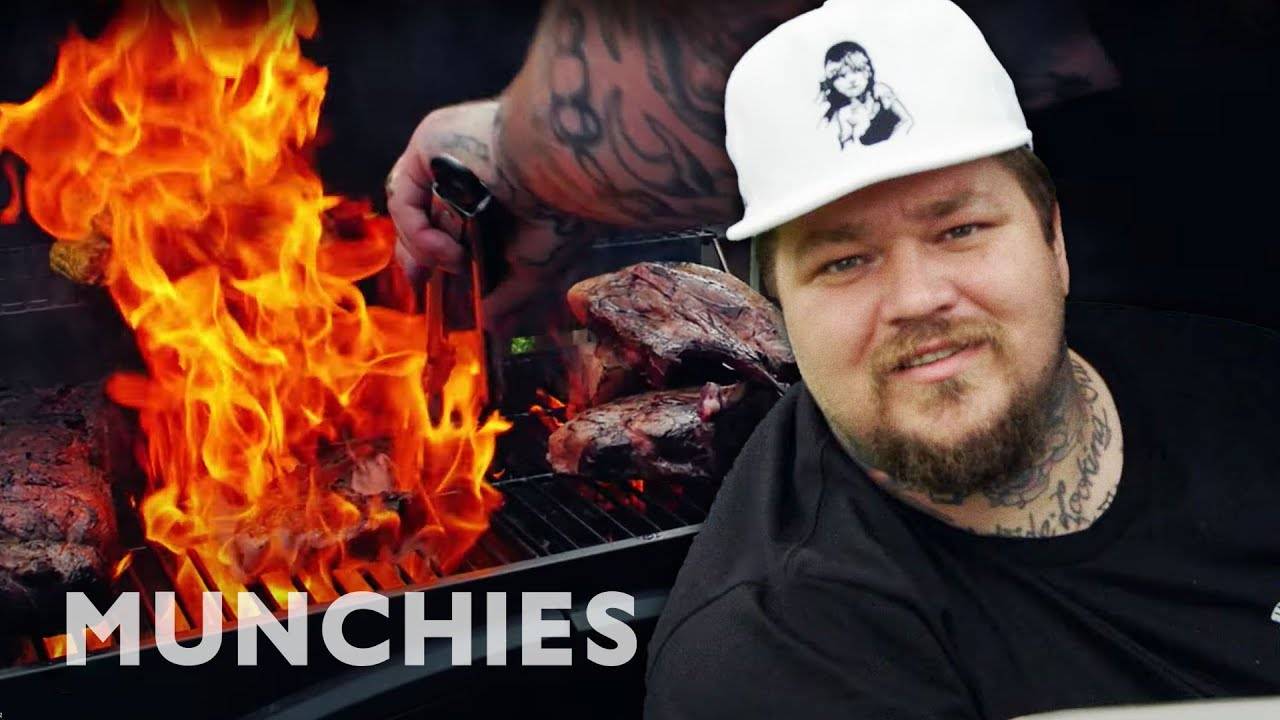 Man grilling steaks over flames with Munchies logo, outdoor barbecue cooking scene