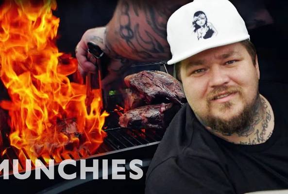 Man grilling steaks over flames with Munchies logo, outdoor barbecue cooking scene